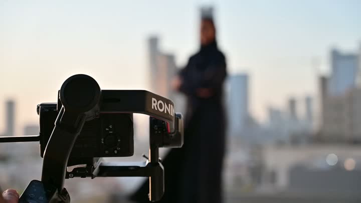 إتقان واحتراف مهنة التصوير، استخدام كاميرا رقمية عالية الدقة، الاهتمام بالأناقة والمظهر الخارجي، مفهوم الأنوثة والنعومة، مصور يقوم بتصوير امرأة عربية خليجية سعودية مبتسمة محجبة ترتدي عباءة تقف بإيماءات السرور والسعادة، خلفية الابراج وناطحات السحاب في الرياض