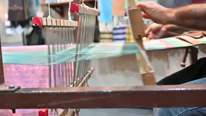 الشغف في ممارسة مهنة الغزل و النسج, تصوير مقرب لرجل عربي خليجي سعودي يقوم بحياكة وغزل الانسجة والقماش, حرفة يدوية تاريخيه, المحافظة على التراث الشعبي السعودي، صناعة المشالح باستخدام الخيوط الملونة