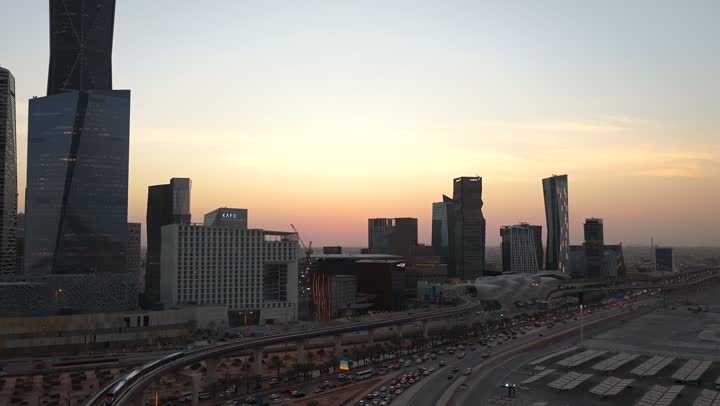 Economic and urban renaissance, aerial drone footage of Riyadh's skyline at sunset, modern and sophisticated towers and skyscrapers, famous commercial and economic landmarks in the Saudi capital, the illuminated King Abdullah Financial District (KAFD)