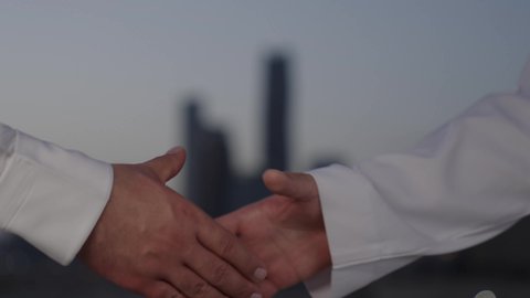 Agreement and partnership on business and commercial projects, acquaintance, friendships and building social relationships, new successful business deals between businessmen, going out in the fresh air, close-up of two men shaking hands, background of towers and skyscrapers