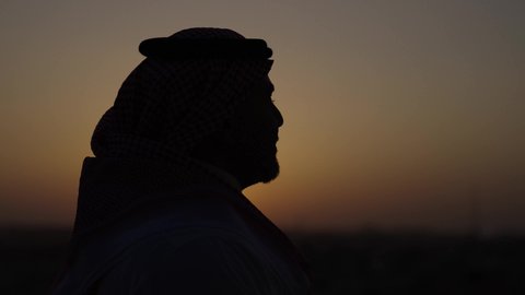 الوقوف بثقة وتأمل المدينة، الوقوف في الهواء الطلق، تصوير مقرب من الجانب لرجل عربي خليجي سعودي يرتدي الثوب والشماغ التقليدي، خلفية غروب الشمس