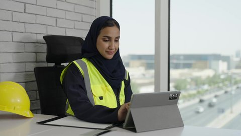 Women's office jobs and professions, the concept of engineering and architectural construction, a Saudi Arabian Gulf female engineer wearing a protective vest working on a tablet, using modern technical devices, using engineering equipment, writing and taking notes, modern and advanced technical devices