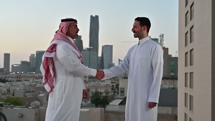 الاتفاق والشراكة على الأعمال والمشاريع التجارية، تعارف وصداقات وبناء علاقات اجتماعية، صفقات عمل جديدة ناجحة بين رجال الأعمال، الخروج في الهواء الطلق، رجلان عربيان خليجيان سعوديان يقومان بمصافحة بعضهما، خلفية الابراج وناطحات السحاب في الرياض