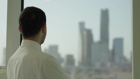 Pride and honor in the Saudi state, towers and skyscrapers of Riyadh, a close-up shot from the side of a Saudi Arabian Gulf man wearing traditional thobe standing inside the building contemplating the city's landmarks, progress and architectural development in the Gulf states