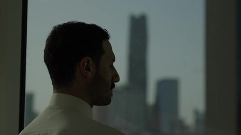 أبراج وناطحات سحاب مدينة الرياض، تصوير مقرب من الجانب لرجل عربي خليجي سعودي يرتدي الثوب التقليدي يقف داخل المبنى يقوم بتأمل معالم المدينة، التقدم والتطور المعماري في دول الخليج