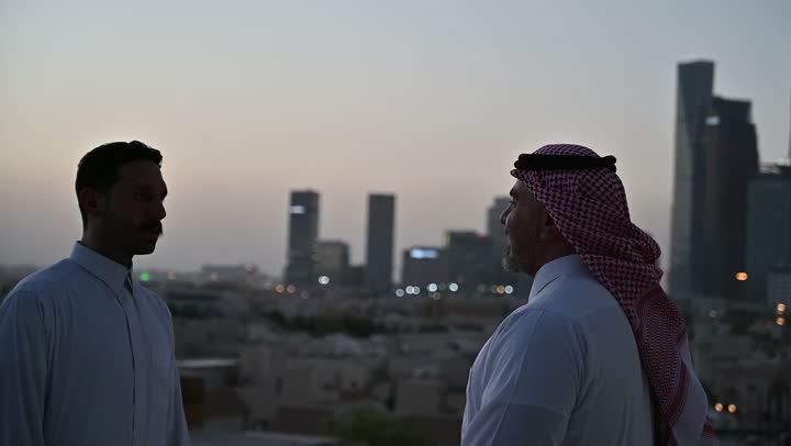 تبادل الأحاديث والاخبار بين الاصدقاء، الاهتمام بالمظهر الخارجي، مفهوم الرجولة والأناقة، رجل عربي خليجي سعودي يرتدي الثوب التقليدي والشماغ يقف مع صديقه بإيماءات الفرح والسرور، خلفية الابراج وناطحات السحاب في الرياض