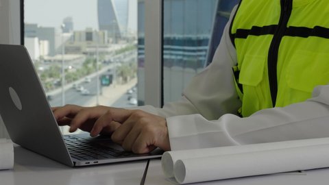 متابعة المشاريع والعمل، استخدام التقنيات الحديثة ومتطورة، الاهتمام بالتطور العمراني بسواعد المهندسين السعوديين, مهندس عربي خليجي سعودي ينجز المهام اليومية في المكتب عبر جهاز الحاسب المحمول ، مفهوم الهندسة والإنشاءات المعمارية، خلفية الأبراج وناطحات السحاب 