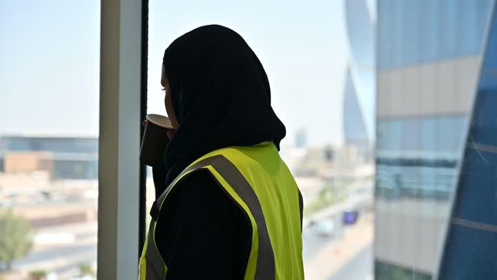 احتساء المشروب المفضل، الافتخار و الاعتزاز بالنهضة العمرانية للمملكة, مشاريع إعمارية سعودية وطنية, مهندسة عربية سعودية خليجية محجبة ترتدي الخوذة وسترة الحماية تحمل بيدها كوب القهوة, بناء الوطن بسواعد أبنائه ومهندسيه, التطور العمراني المتميز للعاصمة