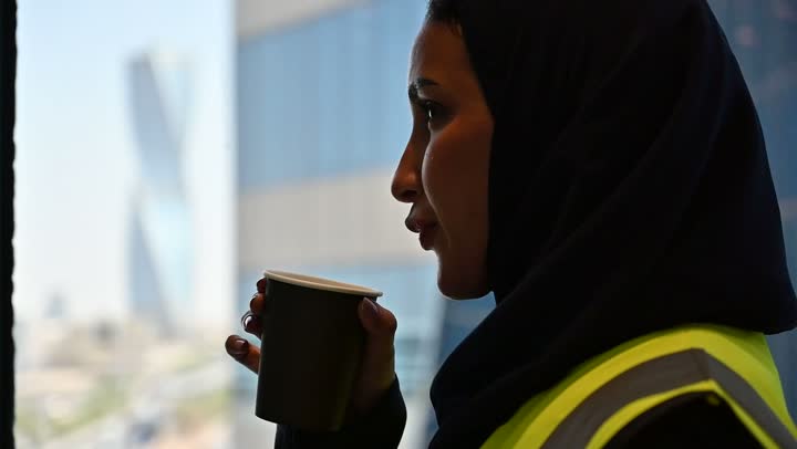 احتساء المشروب المفضل، الافتخار و الاعتزاز بالنهضة العمرانية للمملكة, مشاريع إعمارية سعودية وطنية, مهندسة عربية سعودية خليجية محجبة ترتدي الخوذة وسترة الحماية تحمل بيدها كوب القهوة, بناء الوطن بسواعد أبنائه ومهندسيه, التطور العمراني المتميز للعاصمة