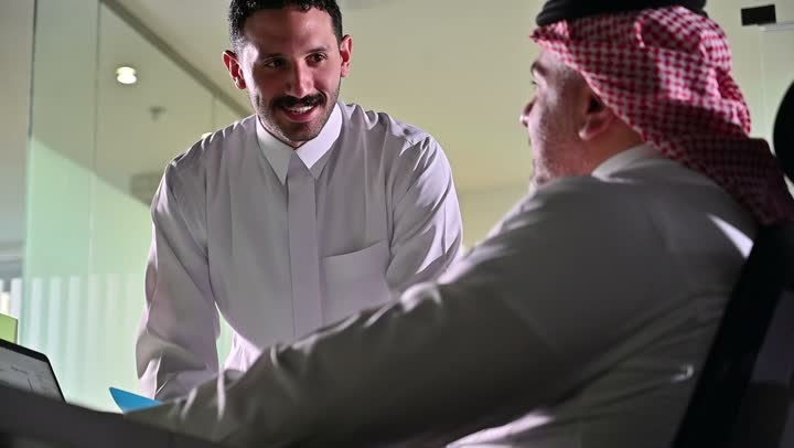 استخدام الحاسب والتقنية في مجال الاعمال، بيئة العمل المريحة في الشركات السعودية، الحوار و النقاش بين الزملاء، تبادل الخبرات والمعلومات لتحقيق الاهداف, موظفان عربيان خليجيان سعوديان يجلسان على مكتبهم داخل مقر الشركة