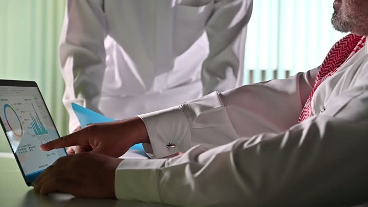 استخدام الحاسب والتقنية في مجال الاعمال، بيئة العمل المريحة في الشركات السعودية، الحوار و النقاش بين الزملاء، تبادل الخبرات والمعلومات لتحقيق الاهداف, موظفان عربيان خليجيان سعوديان يجلسان على مكتبهم داخل مقر الشركة