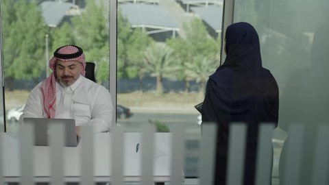 استخدام جهاز تقني حديث، موظفة تقوم بتقديم المشاريع للمدير لتدقيقها عبر الجهاز اللوحي، تطوير ودراسة وتحليل المشاريع الجديدة، موظف عربي خليجي سعودي  يرتدي الثوب والشماغ التقليدي يجلس خلف المكتب داخل مقر الشركة، الوحدة والعمل الجماعي، مهنة ووظيفة سعودية مكتبية