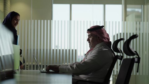 Conducting a meeting for an Arab Gulf-Saudi team at the company's headquarters, developing, studying, and analyzing new projects, unity and teamwork, using a modern technical device, an employee presenting projects to the manager for review, a Saudi office profession and job.