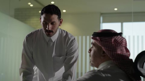 الوحدة والعمل الجماعي، استخدام جهاز تقني حديث، موظف يقوم بتقديم المشاريع للمدير لتدقيقها، تطوير ودراسة وتحليل المشاريع الجديدة، موظف عربي خليجي سعودي  يرتدي الثوب والشماغ التقليدي يجلس خلف المكتب داخل مقر الشركة، مهنة ووظيفة سعودية مكتبية