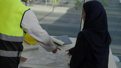 الشركات المختصة بورشات البناء والمقاولات، التخطيط ووضع اللمسات الأخيرة على المخططات المعمارية، تصوير من الخلف لفريق عمل خليجي سعودي يعمل على مناقشة مخطط الإنشاء وتحديد القياسات بدقة، الأعمال الهندسية في المملكة، متابعة تنفيذ الخطط الموضوعة مسبقا