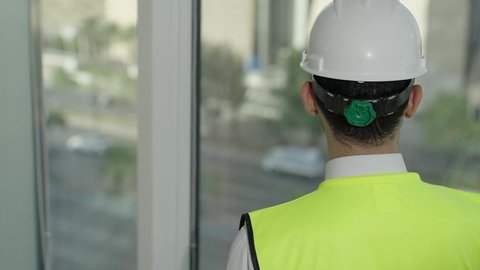 تصوي خلفي بطيئ لمهندس عربي خليجي سعودي يرتدي سترة الحماية والخوذة البيضاء يتأمل معالم المدينة، مفهوم الهندسة المعمارية، المهن والوظائف الشبابية السعودية، تطور ونمو القطاع الهندسي، خلفية حركة المرور