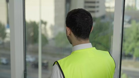 تصوي خلفي بطيئ لمهندس عربي خليجي سعودي يرتدي سترة الحماية والخوذة البيضاء يتأمل معالم المدينة، مفهوم الهندسة المعمارية، المهن والوظائف الشبابية السعودية، تطور ونمو القطاع الهندسي، خلفية حركة المرور