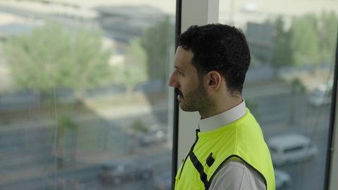 Slow motion side view of a Saudi Arabian Gulf engineer wearing a protective vest and white helmet contemplating the cityscape, concept of architecture, Saudi youth professions and jobs, development and growth of the engineering sector, traffic background