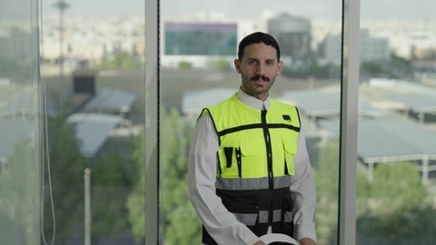 المهن والوظائف الشبابية السعودية، تصويرمقرب لمهندس عربي خليجي سعودي مبتسم يرتدي خوذة بيضاء وسترة الحماية ، مفهوم الهندسة المعمارية،  تطور ونمو القطاع الهندسي، خلفية حركة المرور ومعالم المدينة، الوقوف بثقة والنظر إلى الكاميرا