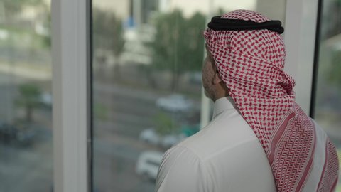 Pride and honor in the Saudi state, close-up from the back of a Saudi Arabian Gulf man wearing the traditional thobe and shemagh standing inside the building contemplating the city's landmarks, progress and architectural development in the Gulf states