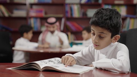 الاستمتاع بقراءة الكتب المدرسية، طالب عربي سعودي خليجيي في المكتبة المدرسية، تأدية الواجبات المدرسية، التعليم في المملكة العربية السعودية