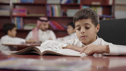 طالب عربي سعودي خليجيي في المكتبة المدرسية، الاستمتاع بقراءة الكتب المدرسية، تأدية الواجبات المدرسية، التعليم في المملكة العربية السعودية