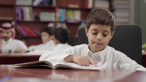 A Saudi Arabian Gulf Arab student in the school library, education in the Kingdom of Saudi Arabia, enjoying reading school books, completing school assignments.