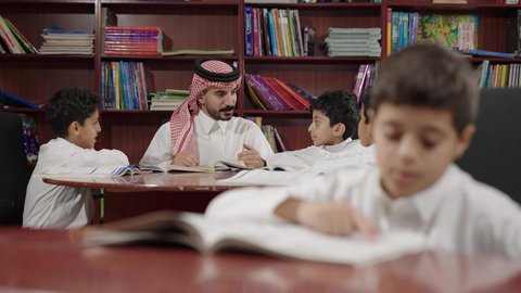Friendly dialogues between the teacher and the student, two Arab Saudi Gulf students in the school library, enjoying reading school books, completing school assignments, education in the Kingdom of Saudi Arabia.