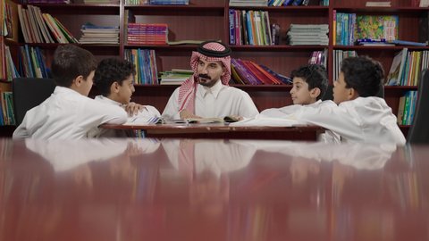 Saudi Arabian Gulf Arab students in the school library, friendly dialogues between the teacher and the student, enjoying reading school books, completing school assignments, education in the Kingdom of Saudi Arabia.