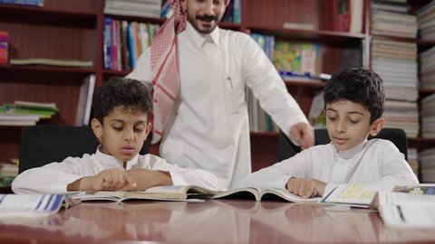 Enjoying reading school books, friendly dialogues between the teacher and the student, Arab Saudi Gulf students in the school library, completing school assignments, education in the Kingdom of Saudi Arabia.