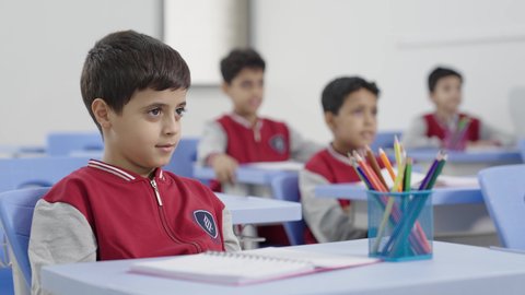 التربية والتعليم بالمناهج المقررة للطلاب في المملكة العربية السعودية، المشاركة والتفاعل داخل الفصل الدراسي،طالب عربي خليجي سعودي يجلس في مقعد يرفع يده للاجاية ،ايماءات الحماس لمعرفة الجواب الصحيح