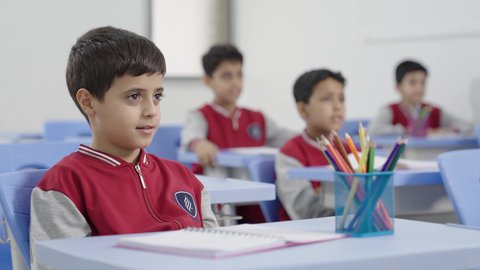 المشاركة والتفاعل داخل الفصل الدراسي،طالب عربي خليجي سعودي يجلس في مقعد يرفع يده للاجاية ، التربية والتعليم بالمناهج المقررة للطلاب في المملكة العربية السعودية،ايماءات الحماس لمعرفة الجواب الصحيح