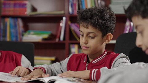 Enjoying reading school books, Arab Saudi Gulf students in the school library, doing homework, education in the Kingdom of Saudi Arabia.
