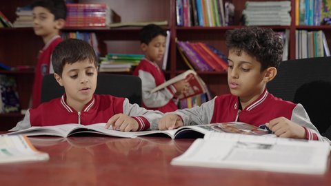 طلاب عربيين سعوديين خليجيين في المكتبة المدرسية، الاستمتاع بقراءة الكتب المدرسية، تأدية الواجبات المدرسية، التعليم في المملكة العربية السعودية