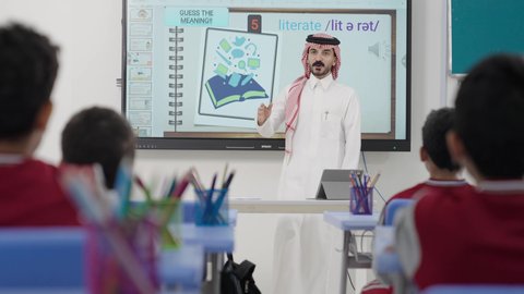Gestures of enthusiasm to know the correct answer, participation and interaction within the classroom, Gulf Arab Saudi students sitting in their seats raising their hands to answer, education and teaching with the curricula prescribed for students in the Kingdom of Saudi Arabia.