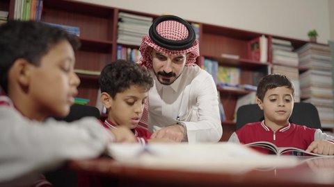 Friendly dialogues between the teacher and the student, Arab Saudi Gulf students in the school library, enjoying reading school books, completing school assignments, education in the Kingdom of Saudi Arabia.