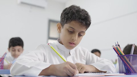 التعليم في السعودية، العودة إلى المدارس، تأدية الواجبات المدرسية، الإستعداد للعام الدراسي الجديد، مجموعة من الطلاب العربيين الخليجيين السعوديين يجلسون في مقاعدهم ويقومون بحل الواجب