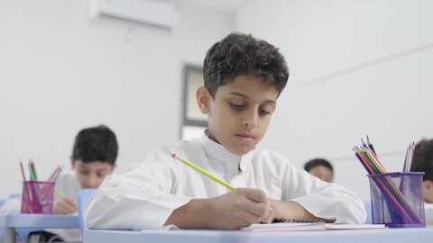 تأدية الواجبات المدرسية، الإستعداد للعام الدراسي الجديد، التعليم في السعودية، العودة إلى المدارس، مجموعة من الطلاب العربيين الخليجيين السعوديين يجلسون في مقاعدهم ويقومون بحل الواجب