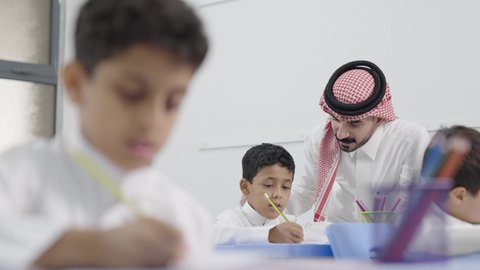 معلم عربي خليجي سعودي يرتدي الثوب التقليدي والشماغ يقوم بمناقشة الدروس مع طلابه، المشاركة الفعالة للطلاب مع المدرسين، جودة التعليم في السعودية، التربية والتعليم بالمناهج المقررة للتلاميذ، حوارات ودية بين الاستاذ والطلاب