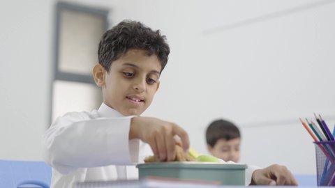 مجموعة من الطلاب العربيين الخليجيين السعوديين  يجلسون في مقاعدهم وأمامهم اللانش البوكس، الاستمتاع بتناول الأطعمة الصحية في وقت الفسحة المدرسية، موسم العودة للمدارس، الوجبات الغنية بالعناصر الغذائية الهامة لبناء الجسم