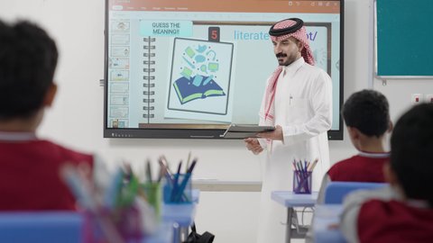 طلاب عربيين خليجيين سعوديين  يجلسون في مقاعدهم وأمامهم طالب يستخدم جهاز التابلت، المناهج المطورة والتعليم الالكتروني، الاستفادة من التقنيات والتكنولوجيا الحديثة في التعلم والدراسة، تطور طرائق التدريس في مدارس المملكة