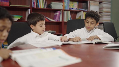تأدية الواجبات المدرسية، مجموعة من الطلاب العرب الخليجيين في مكتبة المدرسة، يستمتعون بقراءة الكتب الدراسية، ويقومون بأداء الواجبات المدرسية، التعليم في المملكة العربية السعودية.