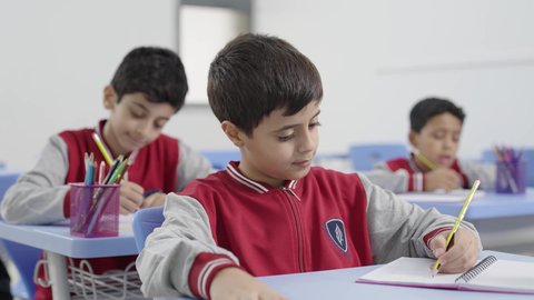 تأدية الواجبات المدرسية، الإستعداد للعام الدراسي الجديد، التعليم في السعودية، العودة إلى المدارس، مجموعة من الطلاب العربيين الخليجيين السعوديين يجلسون في مقاعدهم ويقومون بحل الواجب