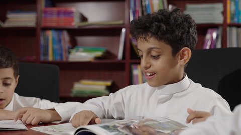 Performing school assignments, a group of Gulf Arab students in the school library, enjoying reading textbooks, and doing their homework, education in the Kingdom of Saudi Arabia.