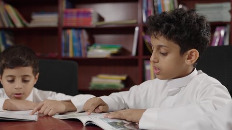 الاستمتاع بقراءة الكتب المدرسية، مجموعة من طلاب عربية سعودية خليجية في المكتبة المدرسية، تأدية الواجبات المدرسية، التعليم في المملكة العربية السعودية