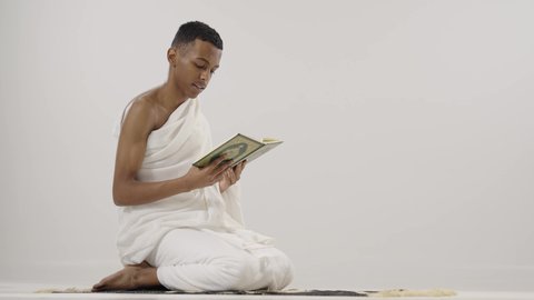 قراءة القرآن الكريم، بورتريه لرجل عربي خليجي سعودي يرتدي لباس الإحرام يحمل بيده المصحف الشريف و يقوم بالتلاوة منه,  الإجتهاد في العبادة, التقرب الى الله تعالى,  مفهوم أركان الإسلام، خلفية رمادي