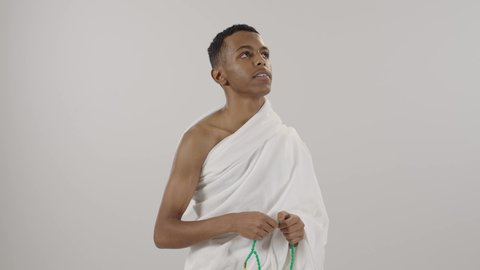 أداء مناسك الحج والعمرة، التهليل والتسبيح وذكر الله تعالى، طلب المغفرة والدعاء والصفح، الاجتهاد في العبادة, قراءة الأذكار والأدعية، بورتريه لرجل عربي خليجي سعودي يرتدي لباس الإحرام يمسك بيده سبحة خضراء، التقرب لرب العالمين، خلفية رمادي