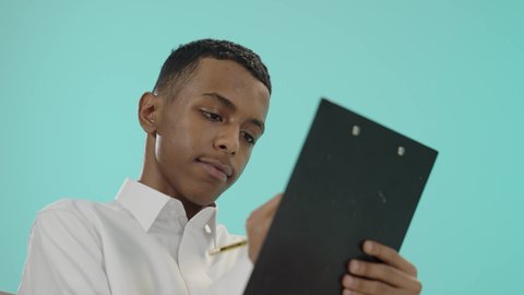 ايماءات التفكير و الحيرة, أدوات تدوين المهام و الملاحظات, بورتريه لرجل عربي خليجي سعودي يرتدي الثوب التقليدي يجلس على كرسي مريح و يقوم بالكتابة على سنادة ورق سوداء، تعابير التمعن والتركيز، خلفية زرقاء