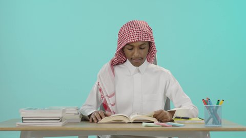 تصفح و قراءة الكتب المفيدة, تعابير الاجتهاد والجد والنشاط، الاستعداد للعام الدراسي الجديد، تحضير الدروس للوصول إلى النجاح, بورتريه لشاب عربي خليجي سعودي يرتدي الثوب التقليدي و شماغ يجلس على الطاولة يقوم بقراءة كتاب, تطوير المناهج التعليمية في السعودية, خلفية زرقاء