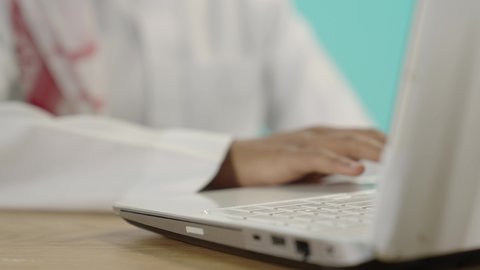 النقر والتفاعل مع لوحة المفاتيح, متابعة حصص الاونلاين عن طريق جهاز الحاسوب، تطوير المناهج التعليمية في السعودية، الاجتهاد وتحضير الدروس, بورتريه مقرب ليد شاب عربي خليجي سعودي يقوم باستخدام اللابتوب في المذاكرة, خلفية زرقاء